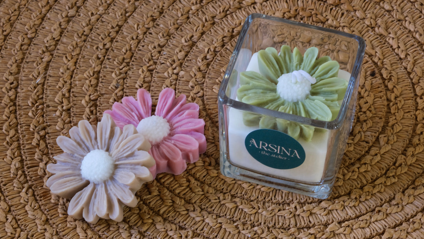 Square glass jar with scented candle and a colorful daisy on top