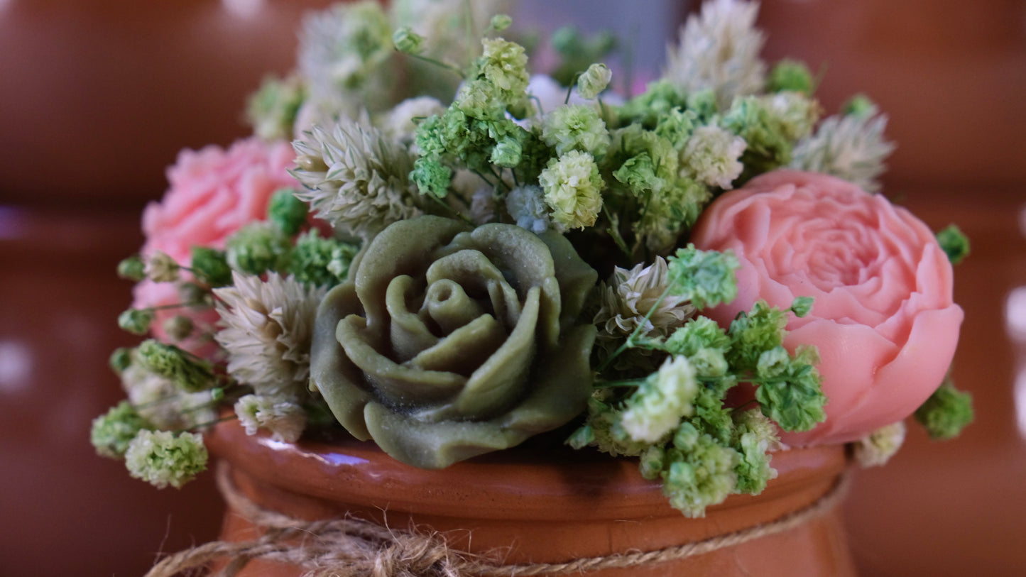 Green and pink scented rose candles in a clay pot